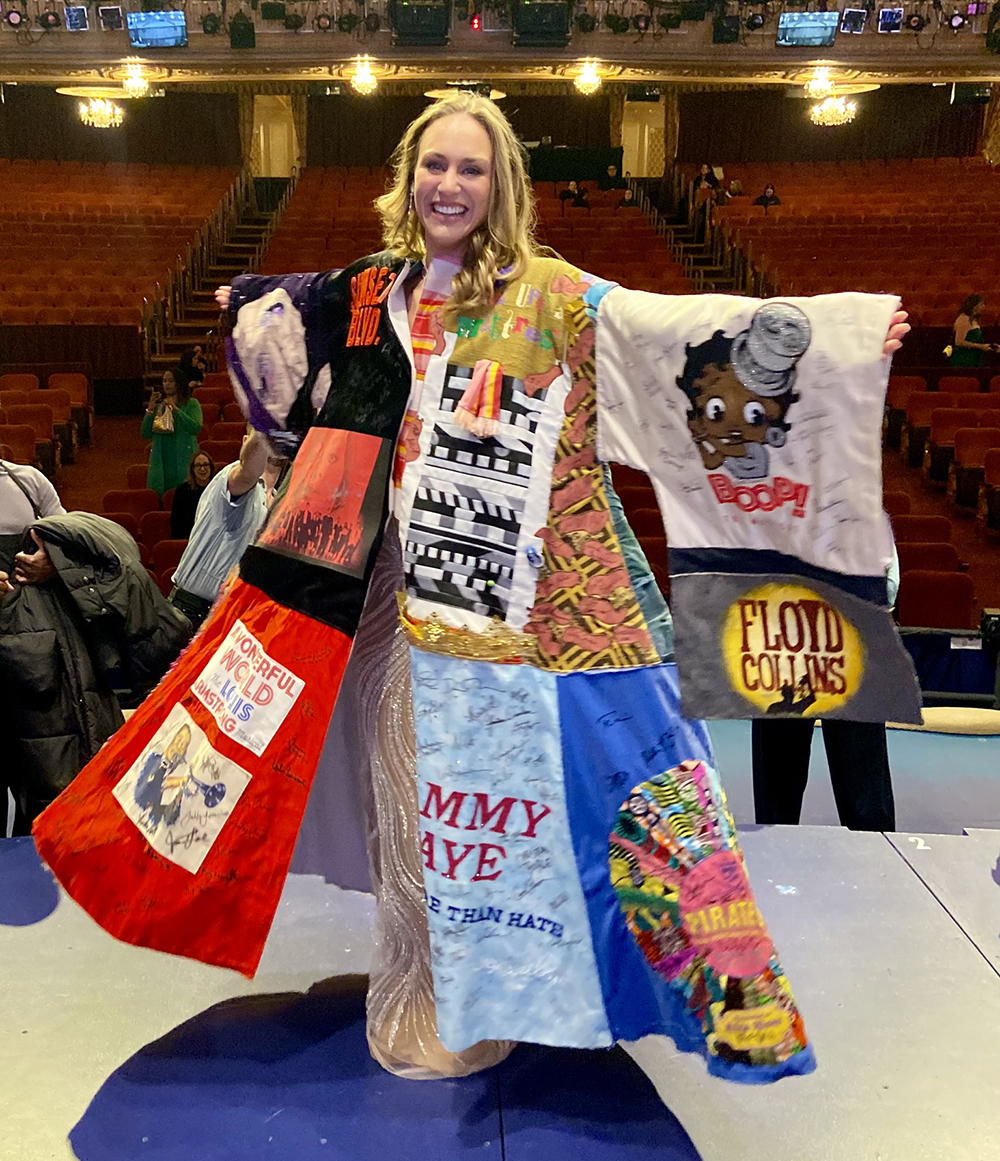 Stephanie Martignetti smiles onstage in the Robe, her arms out and the theater's seats visible behind her.
