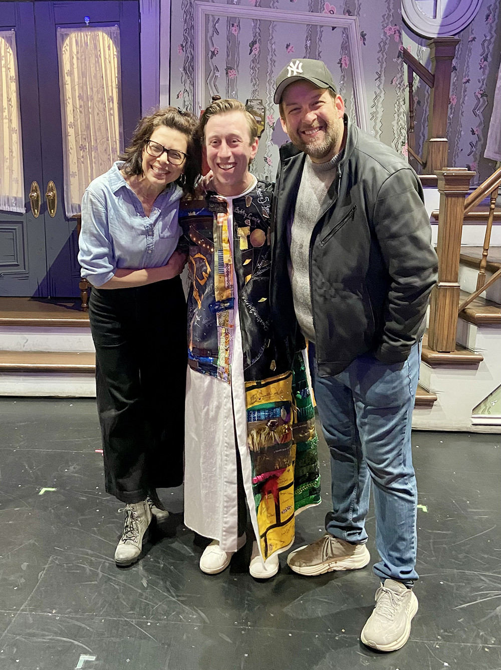 Breslin stands onstage in the Robe, the set visible behind him, flanked by Jill Abramovitz on his left and Andrew Kober on his right. All are smiling.