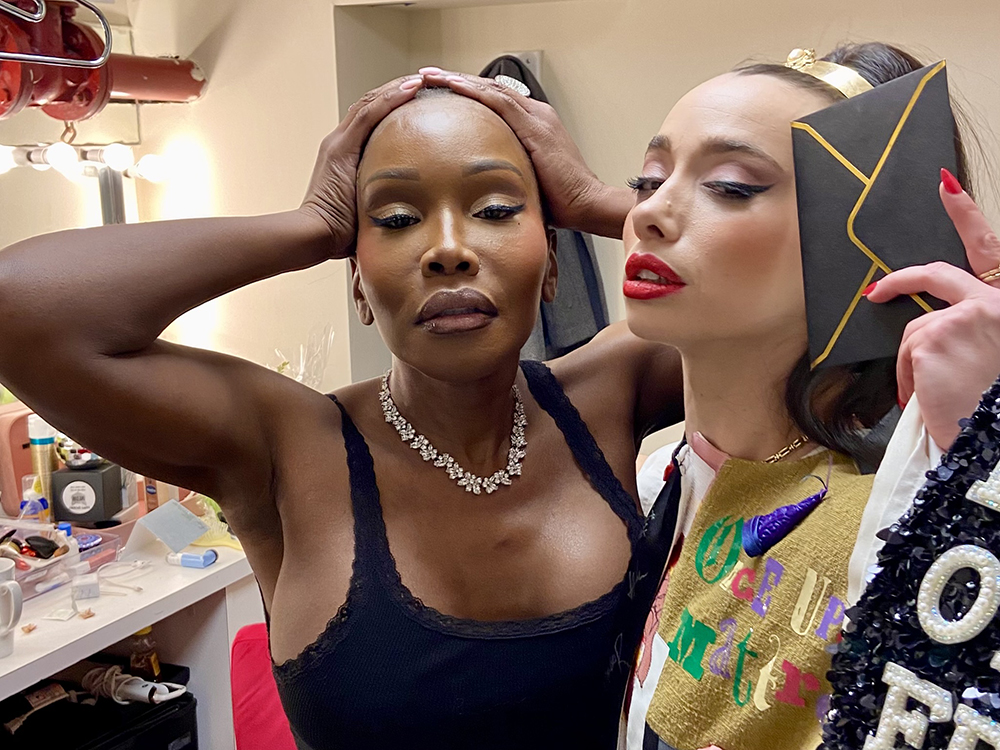 Chasity Moore and Emma Sofia (in the Robe) mug for the camera in the dressing room. Moore has both hands on top of her head and Sofia holds up a pocketbook next to her face.
