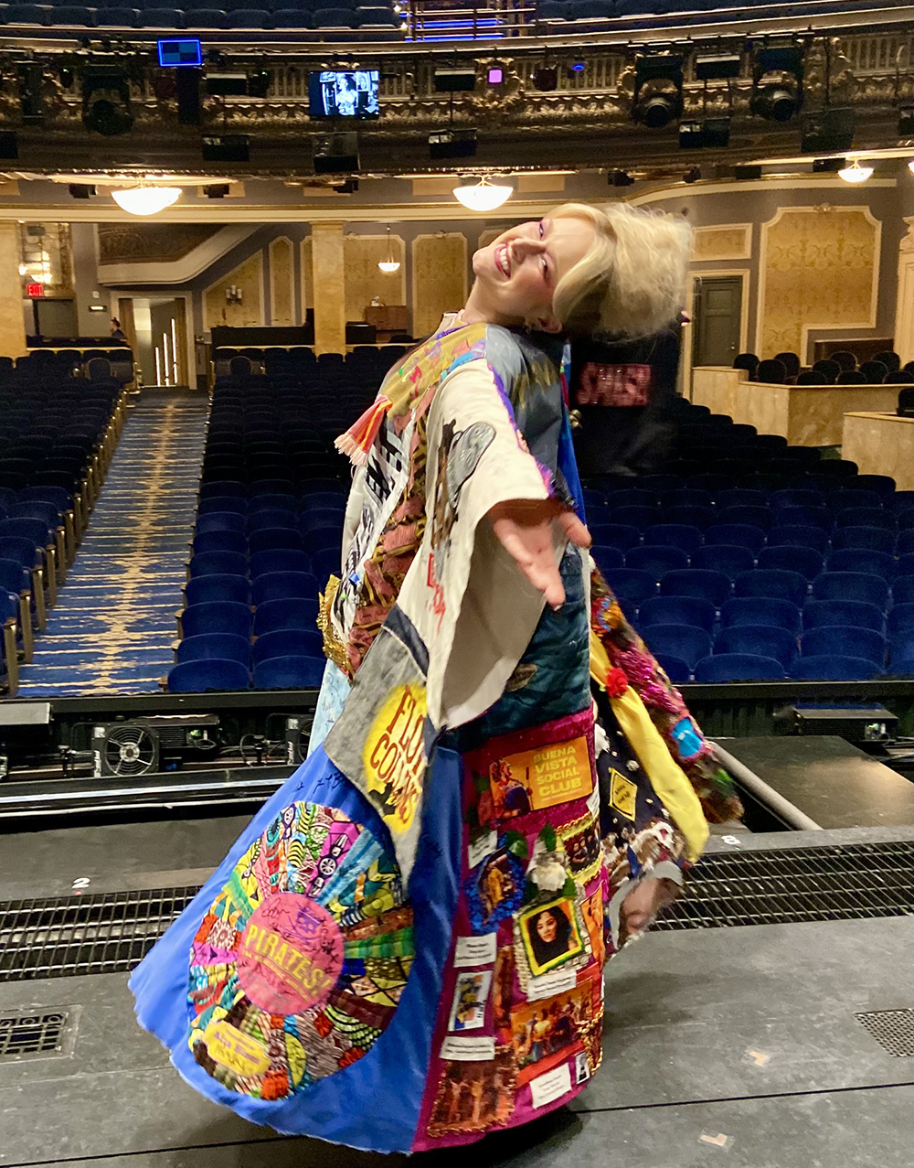 DeLaney Westfall smiles onstage in the Robe with the house behind her. She has her arms out and head tilted back as she spins.