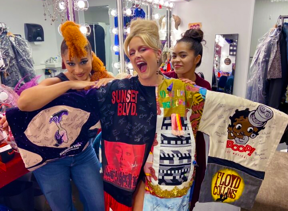 Westfall smiles in a dressing room, wearing the Robe with her arms outstretched. Behind her arms stand Maria Wirries and Jennifer Duka.
