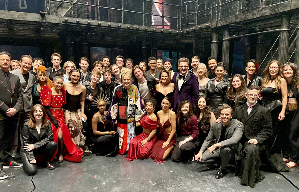 Westfall stands onstage in the Robe surrounded by over 40 people, mostly dressed formally, and smiling for the camera.