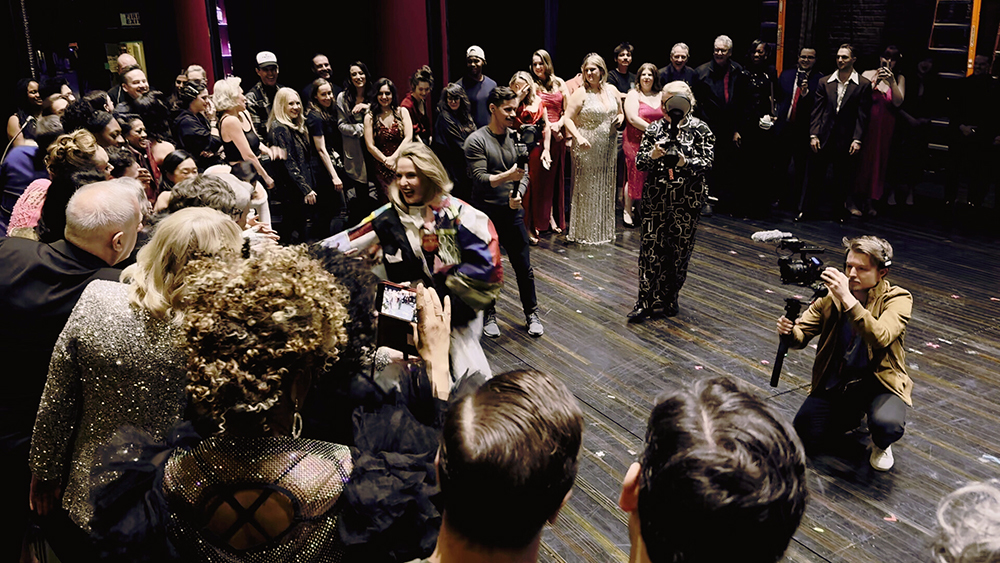 A crowd of people form a circle around Webber as she runs across the stage, hand outstretched to touch some.