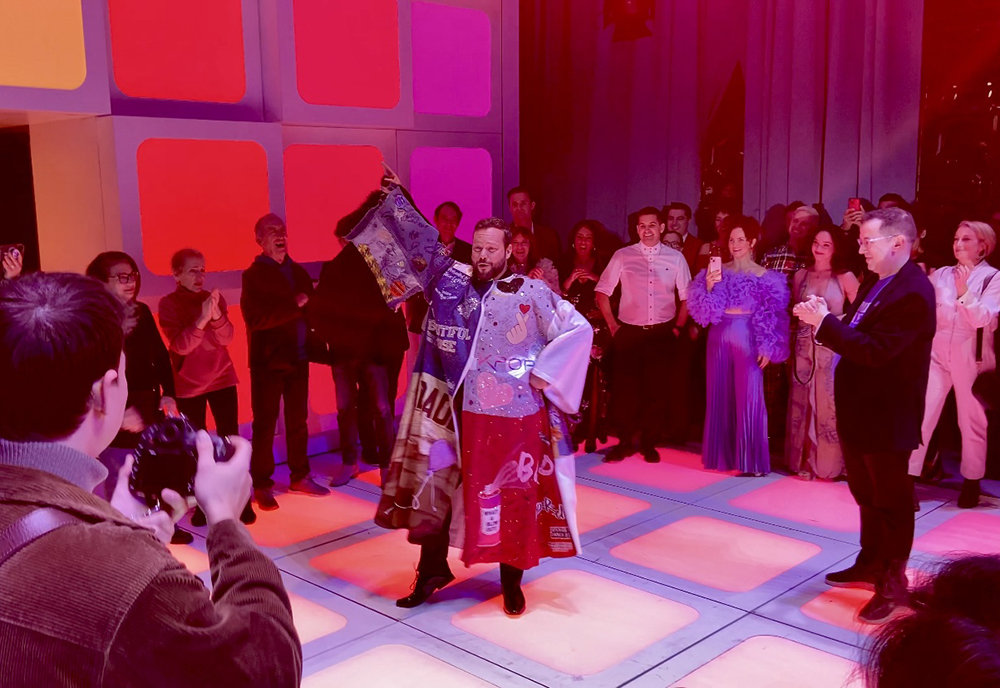 Keven Quillon strikes a pose in the Robe onstage surrounded by a crowd in a circle.