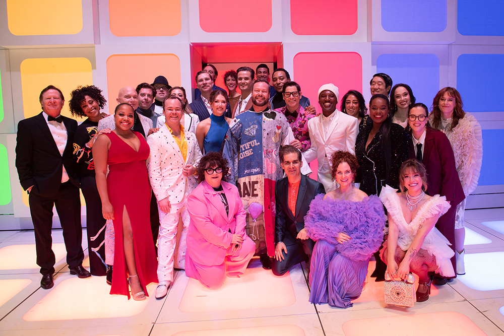 Quillon stands in the Robe onstage surrounded by a couple dozen people posing together.
