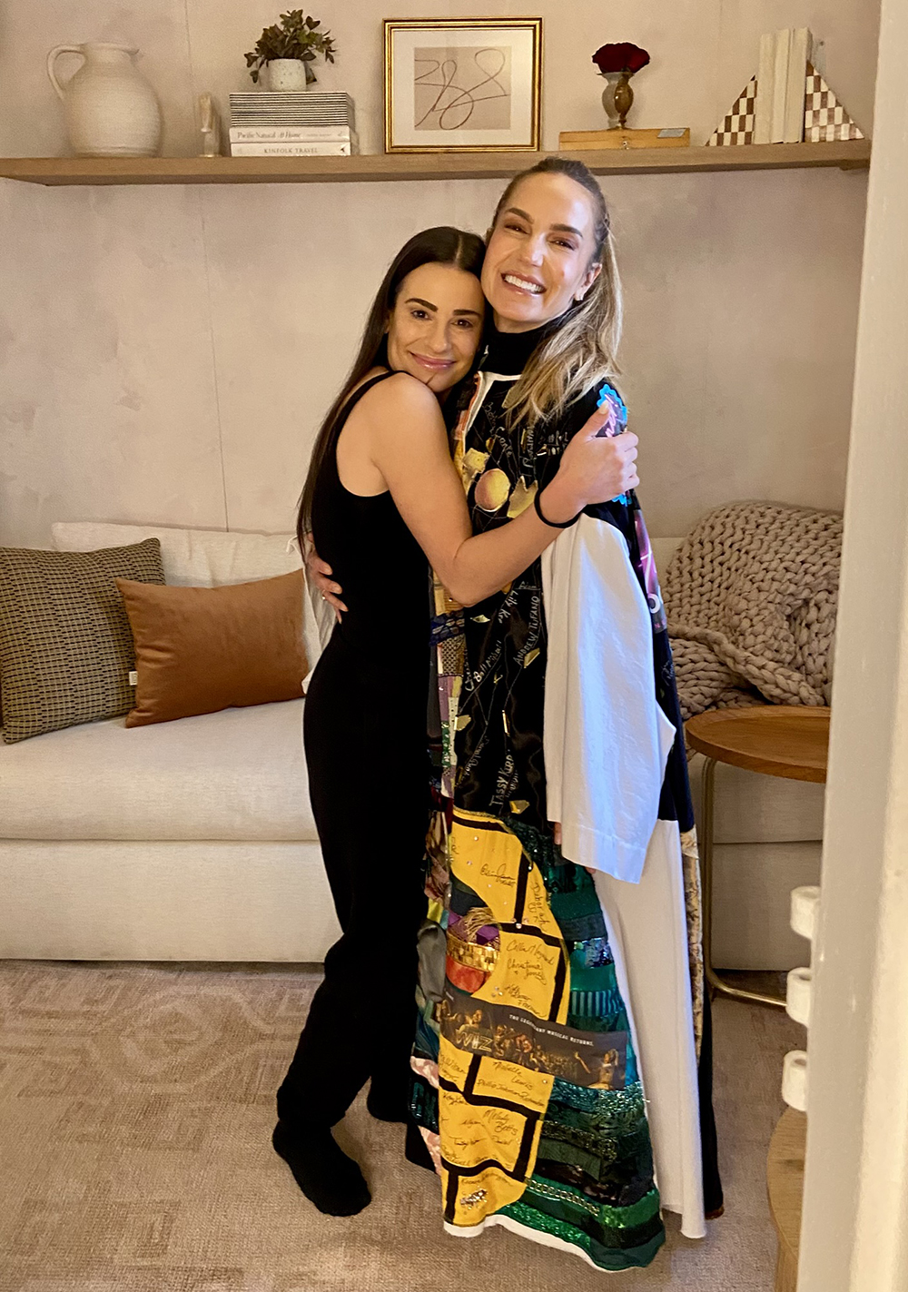Katie Webber wears the Robe while hugging Lea Michele in a dressing room.