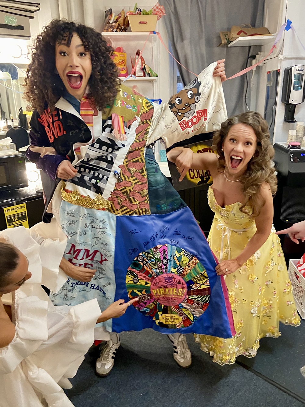 Hines poses in a dressing room, pointing at the 'Pirates!' panel on the Robe. Two castmates, including Maria Briggs, point excitedly as well.